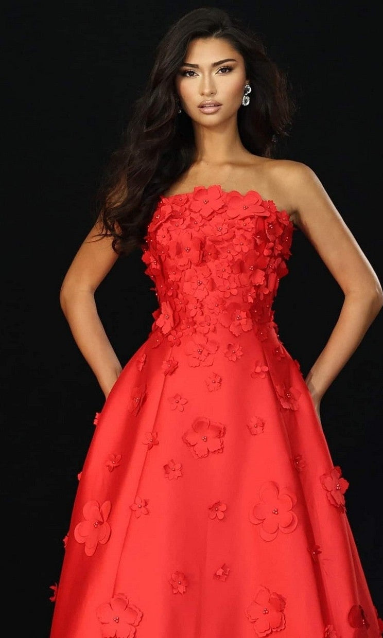 A woman models the Jovani 48444 long prom dress, featuring a red strapless design with 3D floral appliques, set against a black background.
